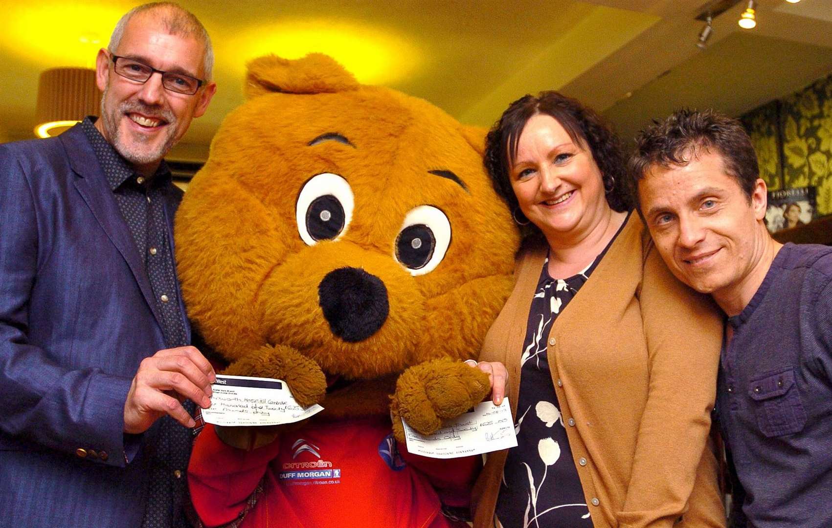 Winners of the KLFM Balloon Race are David and Louise Auker with the two cheques, both for £625, which they donated to Papworth Hospital and Cystic Fibrosis Trust. Also with them is KLFM presenter Simon Rowe and Super Trooper Bear