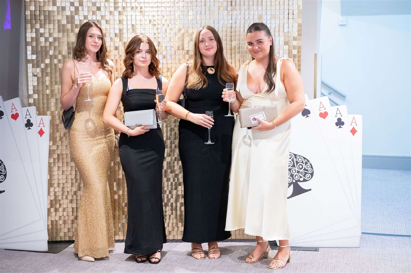 Friends pose in front of sequinned wall at the prom